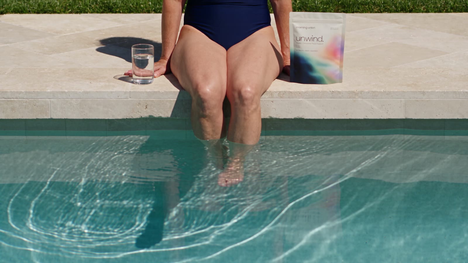 A woman at the pool edge with a pouch of unwind. beside her